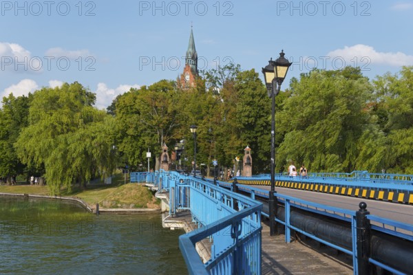 Blue bridge against a lush green backdrop with church tower and lanterns in sunny weather, historic bridge, Elk, Elk, Lyck, Jezioro Elckie, Warmia-Masuria, Poland