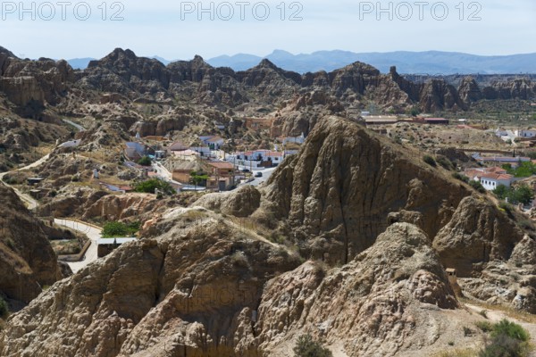 A small village nestled in a rocky, rugged landscape under a sunny sky, view from the Mirador del Cerro de la Bala, cave dwellings, cave district, Troglodytos, Barrio de Cuevas, Guadix, Granada province, Andalusia, Spain
