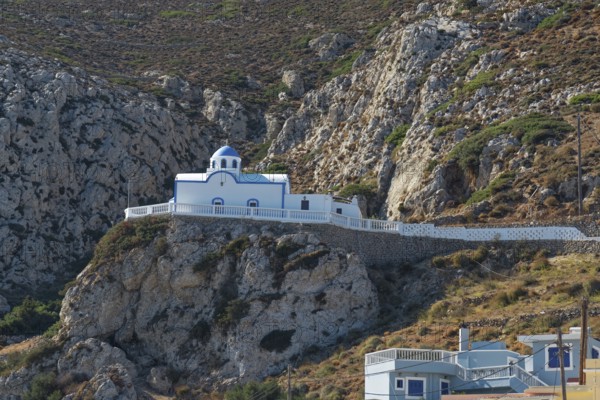 White chapel of Agios Spiridonas with blue roof on a stony rock surrounded by mountains, Menetes, Karpathos, Greece
