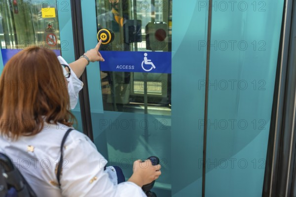 Woman using a wheelchair is pushing accessible button to enter public transport, promoting inclusivity and independent mobility