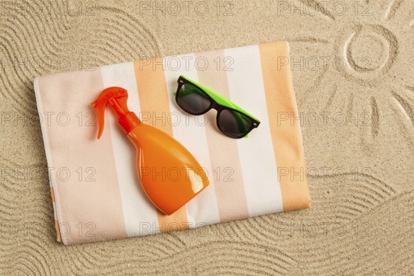 Drawing on the sand, sun and waves, sunglasses, with an orange bottle, beach towel, sun spray, on the sand, top view, no people
