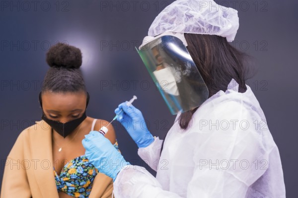 Black woman receiving the injection of the coronavirus vaccine by a doctor, antibodies, immunizes the population, people at risk, antibodies, new normal, covid-19