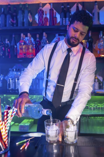 Professional bartender preparing cocktails, pouring alcoholic beverage into glasses with ice at bar counter in nightclub