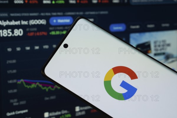 Google logo is displayed on a smartphone screen, with a stock graph webpage visible on a computer screen in the background