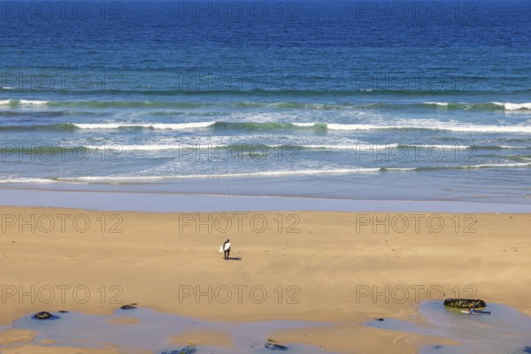 Man with a surfboard walking up from the water with breaking waves on a sand beach, Crozon peninsula, Bretagne, France