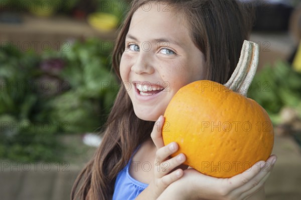 Happy young blue eyed girl holding a fresh pumpkin at the farmers market