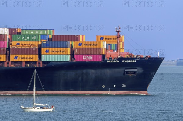 Sailboat sailing past bow of container ship, containership Hudson Express of the Hapag-Lloyd AG shipping company loaded with containers