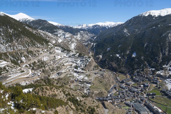 Verschneite Berge und ein Tal mit Straßen und verstreuten Gebäuden unter einem klaren blauen Himmel in Andorra, Mirador del Roc del Quer, Blick auf Canillo, Fürstentum Andorra, Pyrenäen