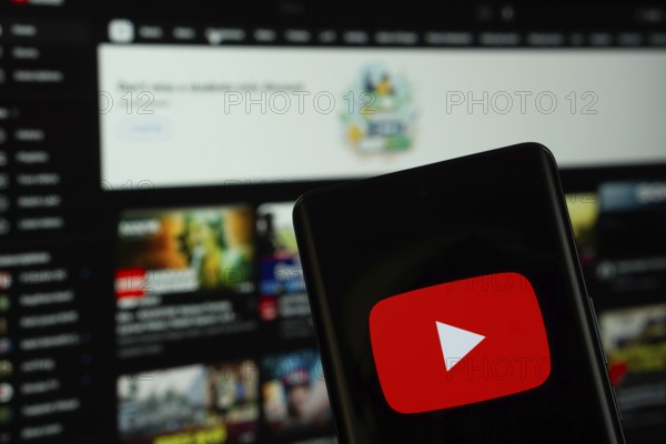 Dhaka, Bangladesh- 10 July 2025: Youtube logo is displayed on a smartphone screen, with the website visible on a computer screen in the background