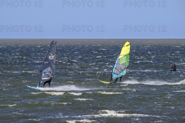 Kiteboarder, kitesurfer and two recreational windsurfers in wetsuits practising classic windsurfing along the North Sea coast in windy weather