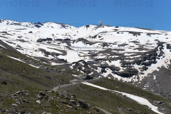 Snow-covered mountains under a bright blue sky with rocky landscape in the foreground, view of mountains of Hoya de la Mora, basin of the Maurin, Güéjar Sierra, Güejar, Sierra Nevada, Andalusia, Spain