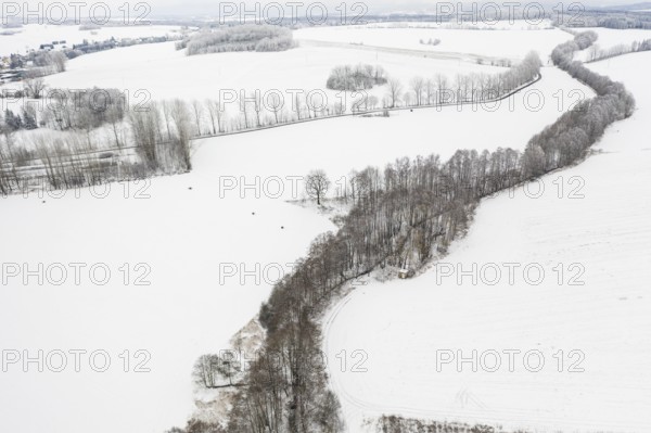 Aerial view of a winding tree-lined stream in the snow, between Eppendorf and Leubsdorf, Central Saxony, Germany