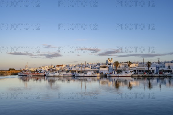 View of Naoussa, Fishing boats in the harbour at sunset, reflected in the sea, White Cycladic houses and church Agios Faneromeni, Naoussa, Paros, Cyclades, Greece