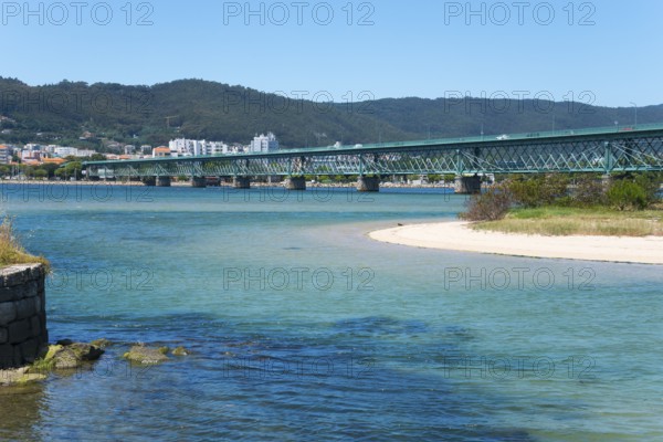 A long bridge crosses a shimmering blue river, surrounded by hills and a town in the background, Ponte Eiffel, Bridge by Gustave Eiffel, Lima River, Viana do Castelo, Portugal