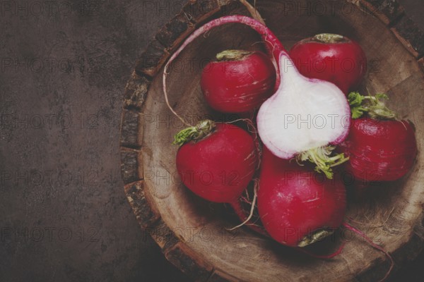 Fresh red radishes are displayed on a rustic wooden cutting board, highlighting their smooth skins and crisp white interiors. The vegetables are vibrant and inviting