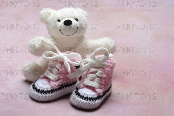 Pink baby shoes with teddy bear, pink background