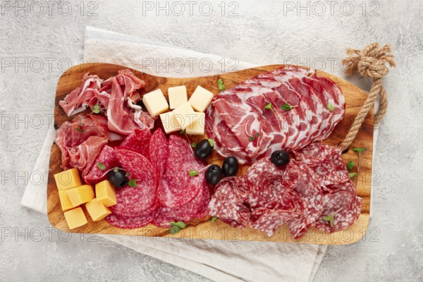 Assorted, sliced meat appetizer, prosciutto, salami and ham, with cheese and olives, on a wooden board, breakfast, top view, close-up, no people