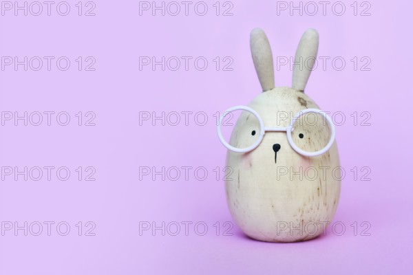 Cute funny egg shaped Easter bunny with glasses on pink background with copy sapce