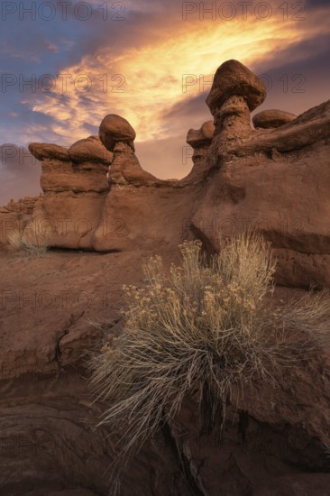Stunning sandstone formations at Goblin Valley State Park, Utah, bask under a dramatic sunset. The vivid sky illuminates unique rock shapes, capturing nature's artistry