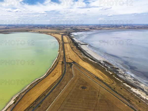 Aerial photo contrasting vibrant green and gray lakes divided by roads and golden fields in Victoria, Australia. Cloudy sky adds depth to this serene landscape, highlighting nature beauty