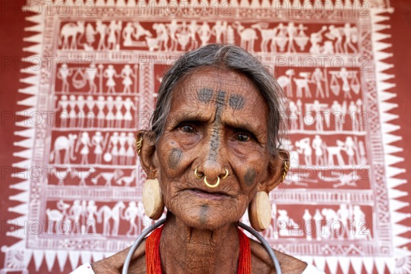 Portrait of a woman from the Lanjia Saora tribe (Odisha, India) . Behind her, a Lanjia Saora traditional mural painting
