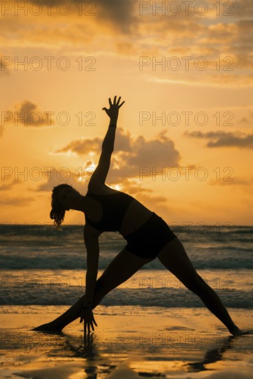 A serene silhouette of a woman practicing yoga on a beach during sunset in Tulum, Mexico. The warm glow of the sun reflects off the sand, creating a peaceful atmosphere
