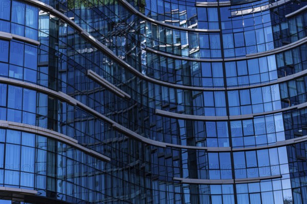 A close-up view of a modern building showcasing a curved glass facade with visible reflections and metal frames, illustrating the use of concrete, glass, and metal in contemporary architecture