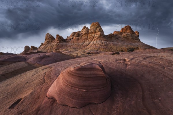 A breathtaking view of Coyote Buttes in Paria Canyon-Vermilion Cliffs Wilderness, Arizona, under stormy skies. The dramatic clouds and a striking lightning bolt accentuate the unique red rock structures
