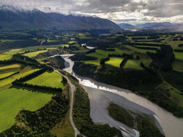 Aerial view of Canterbury region's lush green farmland and winding river, nestled against the backdrop of snow-capped mountains, capturing the essence of New Zealand's natural beauty