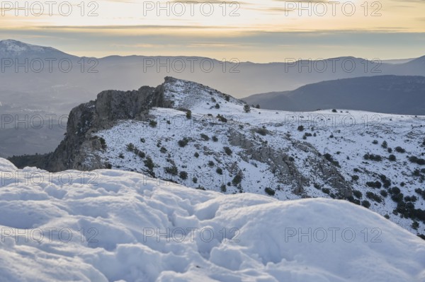 Scenic view of Montcabrer, Spain, showcasing its snow-covered peaks under a softly glowing sunrise. The tranquil landscape captures the serene beauty of winter