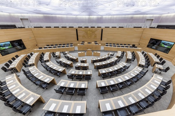 Plenary hall deserted with the seats of deputies and the government bank. Behind it is the coat of arms of the federal state. The state parliament of Baden-Württemberg is the state parliament based in Stuttgart, Baden-Württemberg, Germany