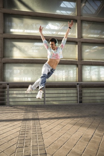 A joyful dancer in a colorful cropped top and jeans leaps gracefully, wearing headphones and sneakers. The urban industrial setting enhances the vibrant energy and motion