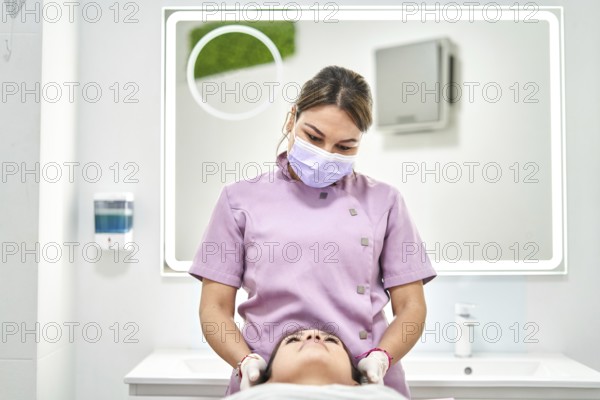 A skilled practitioner wearing a mask provides a facial treatment to a client in a modern beauty salon. The setting is clean and bright, emphasizing skincare and relaxation