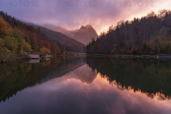 A stunning sunset at Riessersee in the Bavarian Alps casts vivid colors over calm waters, beautifully reflecting the surrounding autumn foliage and distant mountains