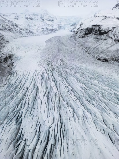 Aerial view of Icelandic winter landscape featuring a vast, icy glacier with intricate patterns. The remote, wild nature showcases snow-covered peaks and cold, rugged terrain, Ã–rÃ¦fi, Austurland, Islandia