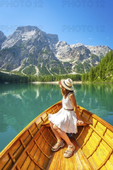 Woman wearing summer dress and hat enjoying boat trip on the alpine lake in dolomites mountains
