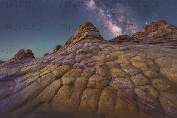A breathtaking view of the Milky Way illuminating a unique, textured rock formation in Coyote Buttes, Arizona. The night sky is filled with stars, showcasing nature wonder