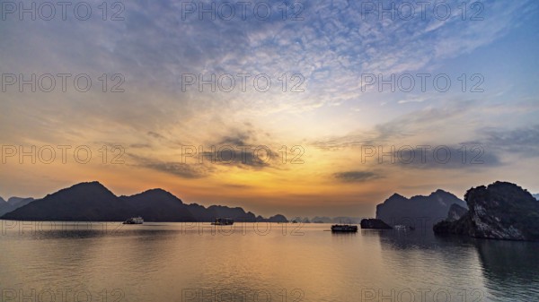 Wide sky at sunset over still water and distant rocks, sunset in Halong Bay, Vietnam