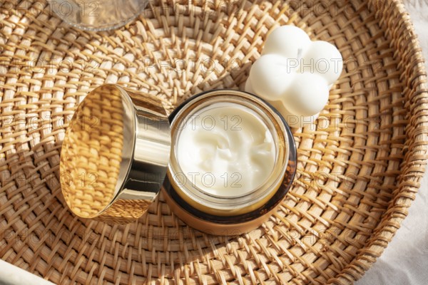 A luxurious skincare cream in an elegant gold jar, placed on a woven rattan tray beside a white decorative candle, highlighting beauty and self care