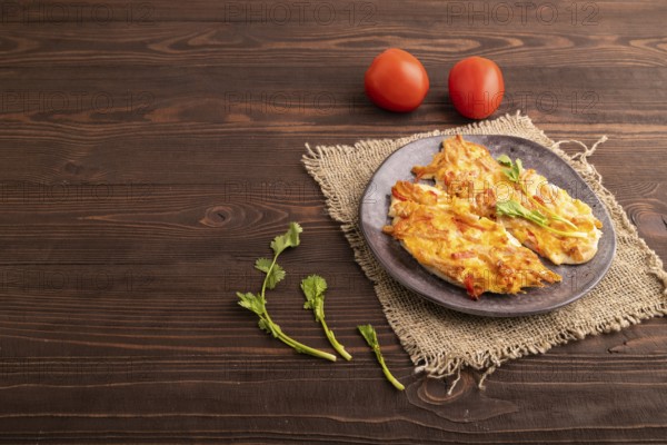 Baked chicken meat with cheese and tomatoes on brown wooden background and linen textile. side view, copy space