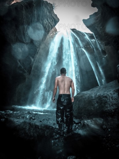Adventurous young man under Gljufrafoss waterfall in winter in Iceland