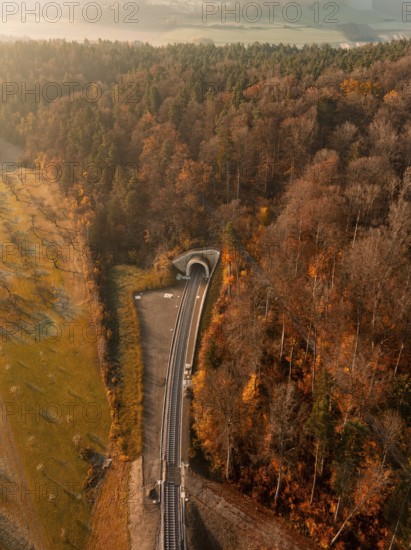 Aerial view of a forest in autumn with tracks and a tunnel illuminated by warm sunlight, new tunnel of the Hermann Hesse Railway, Weil der Stadt. Germany
