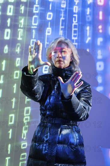 An elderly Asian woman with virtual reality glasses interacts in a digital metaverse environment. She stands confidently amidst a backdrop of binary code and futuristic elements