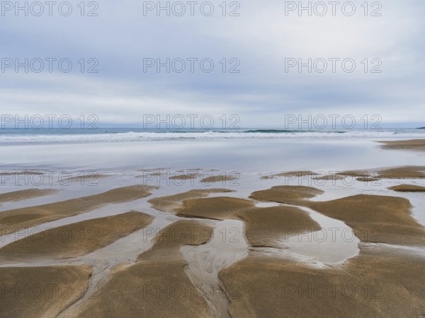 Serene coastal landscape featuring expansive sandy shores and reflective tidal pools under a cloudy sky, conveying the beauty and calm of nature