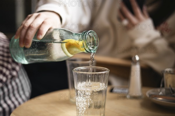 Cropped unrecognizable girl pours water from a bottle with a slice of lemon into a glass in a cafe, capturing a moment of refreshment