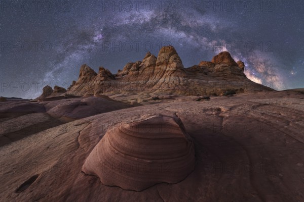 An awe inspiring view of the Milky Way galaxy illuminating the night sky above a rugged desert landscape with striking rock formations in Coyote Buttes, creating a breathtaking celestial scene
