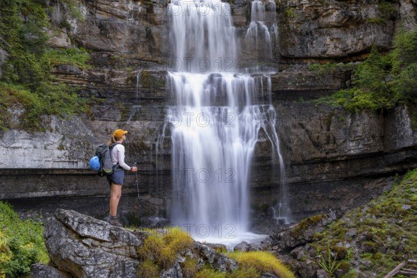 Young pretty hiker standing on rocks in front of Cascata di Mezzo waterfall, long exposure, Vallesinella, Brenta, Trentino, Italy