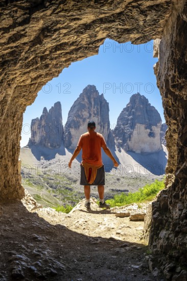 Tourist enjoying the breathtaking view of the tre cime di lavaredo, framed by a natural Tre Cime Cave entrance, during a summer hike in the italian dolomites