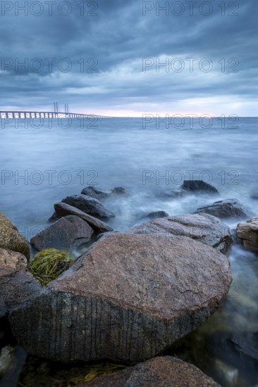 Rocks in the foreground lead to a bridge running across the sea in the distance, Öresund Bridge, Øresundsbroen, the world's longest cable-stayed bridge, connecting Copenhagen with Malmö