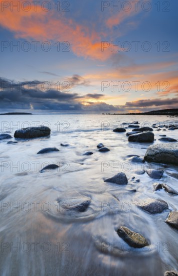 Orange coloured cloudy sky at sunset on a sandy beach strewn with round stones near Achiltibuie on the west coast of Scotland